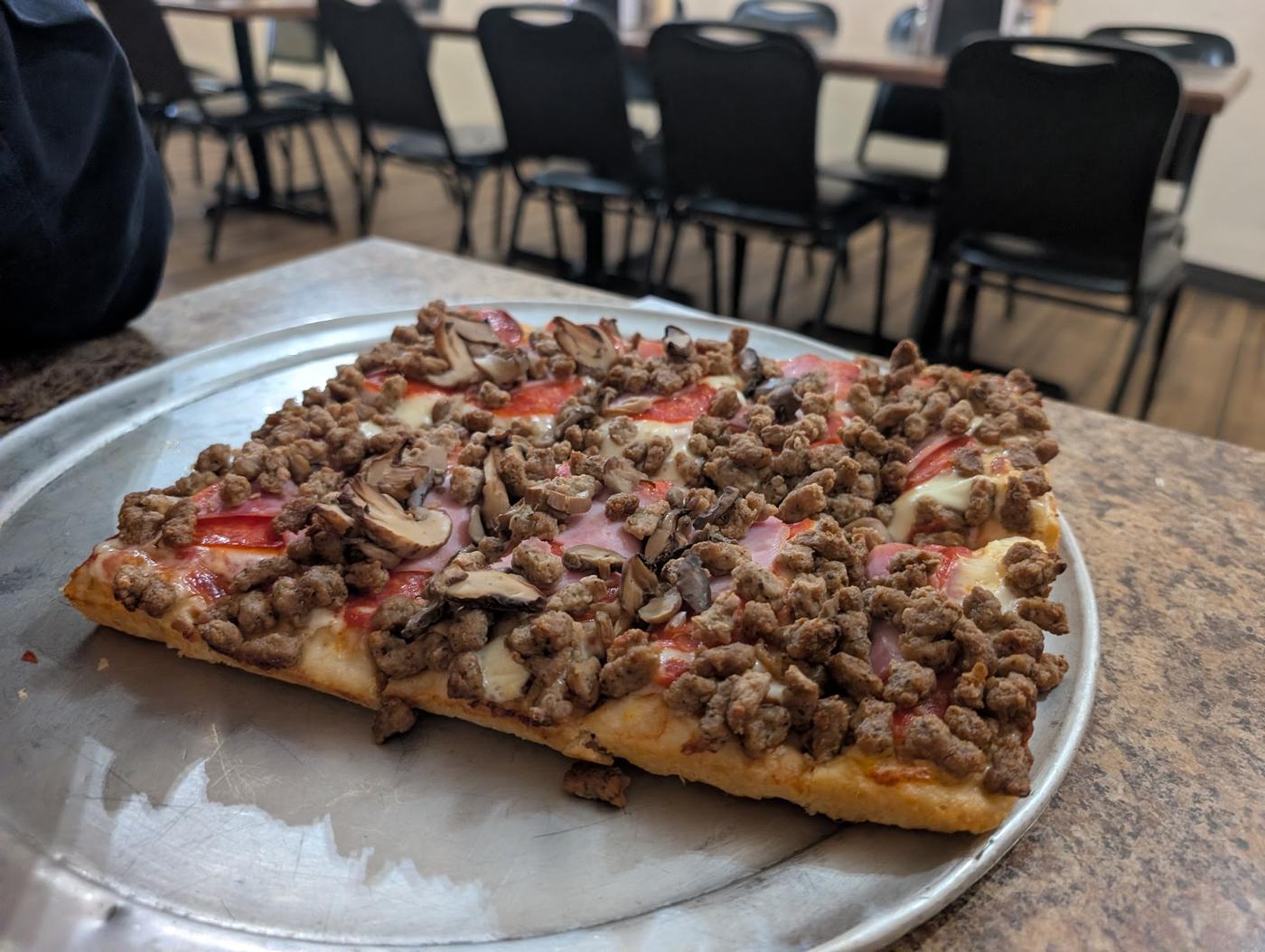 A loaded sausage and mushroom pizza on a metal pan, with the dining room behind it