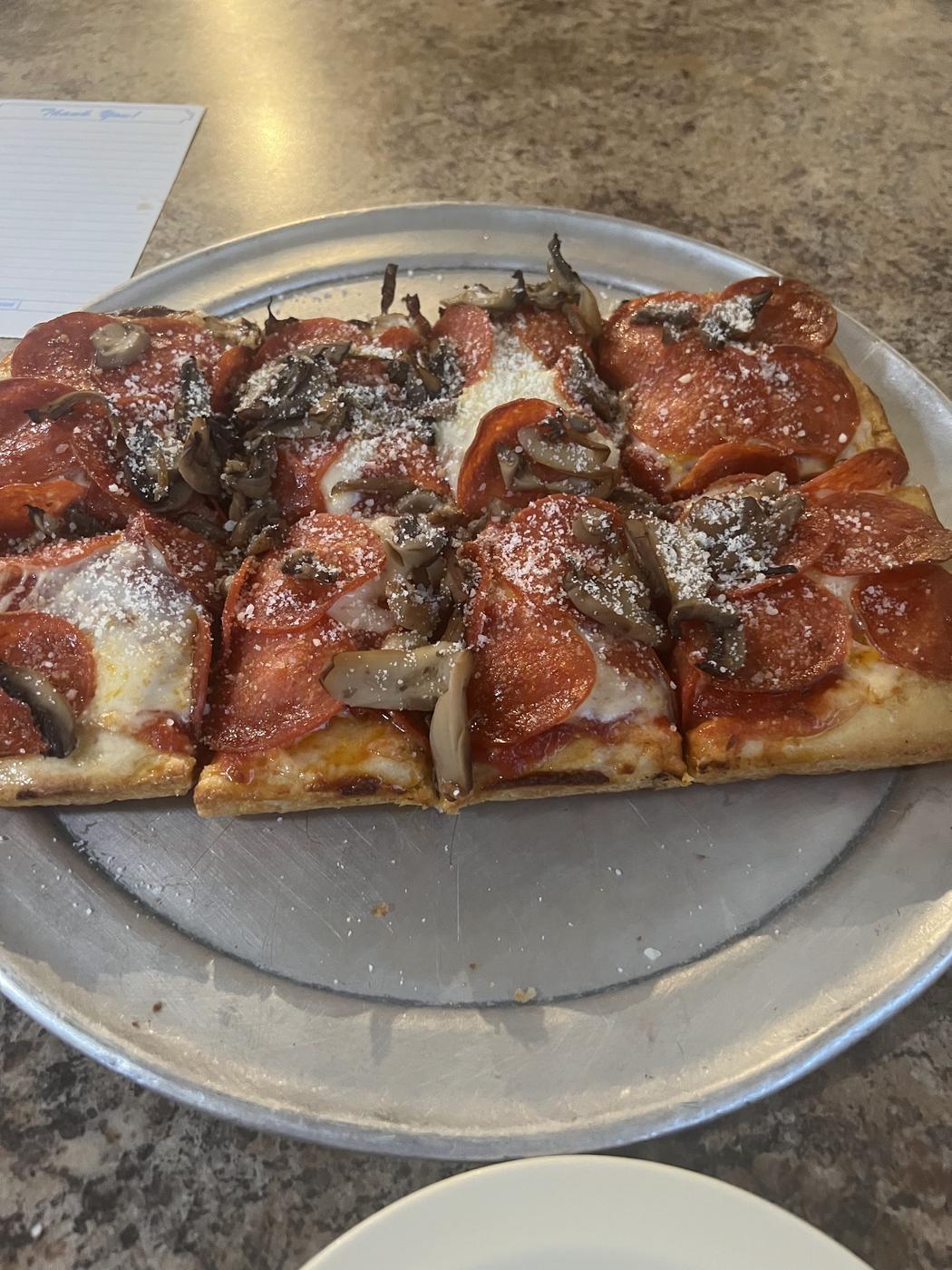 A thin crust pepperoni and mushroom pizza, cut into squares on a metal pan